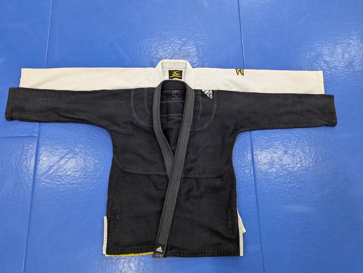 A black jiu-jitsu jacket laid on top of a white judo-cut jacket