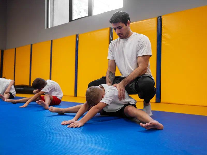 A coach helping children stretch on the mat
