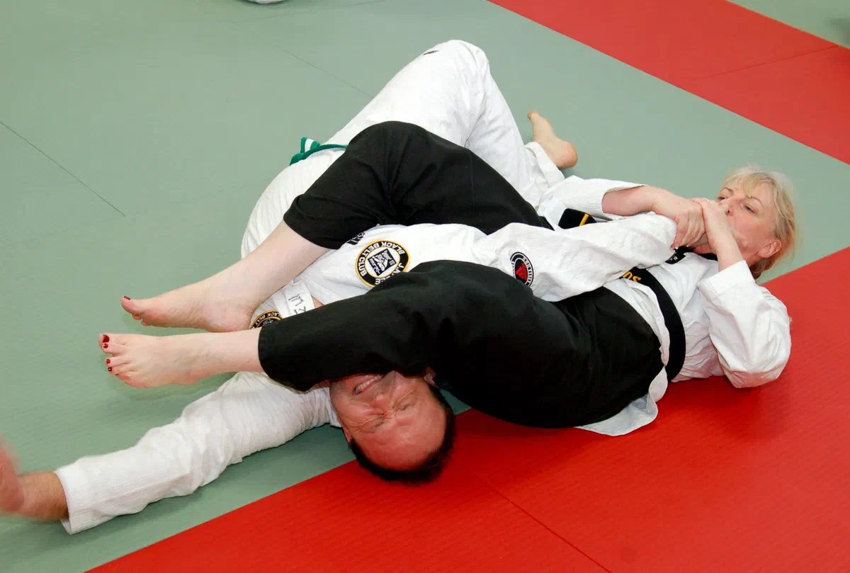 A woman in a white gi finishing an armbar on a man in a black gi